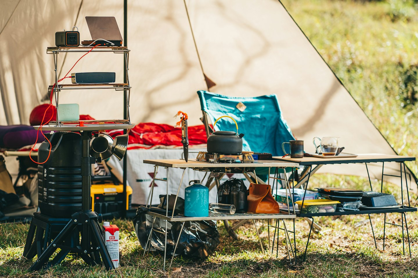 Attrezzatura da campeggio organizzata su mensole e tavoli fuori da una tenda.