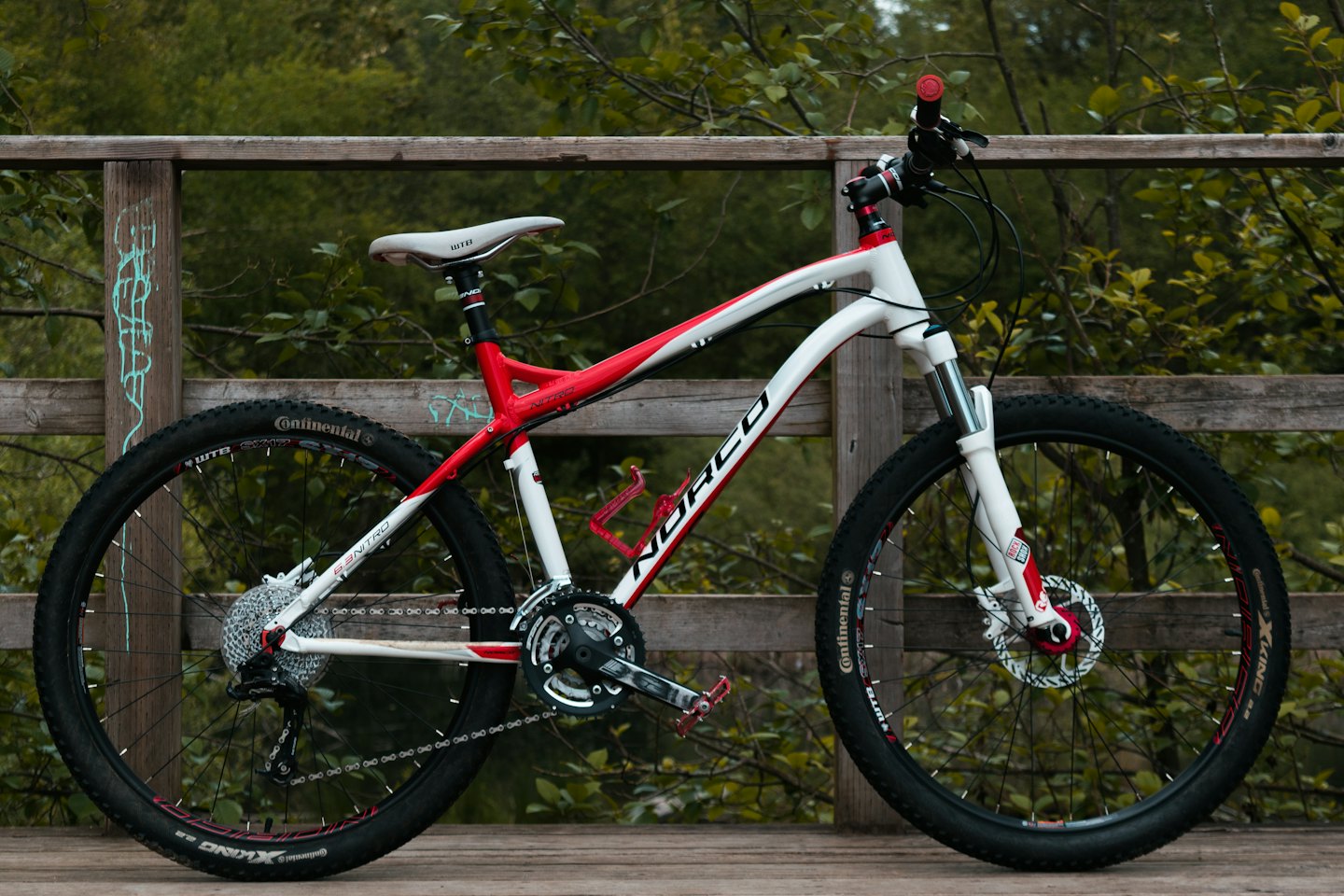 Bicicletta da montagna rossa e bianca appoggiata a una staccionata di legno.