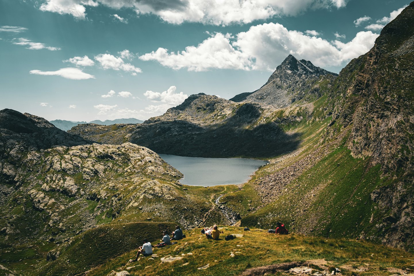 Escursionisti che riposano su un pendio erboso con vista su un lago di montagna.