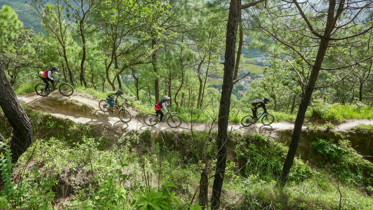Quattro mountain biker percorrono un sentiero sterrato tortuoso nel bosco.